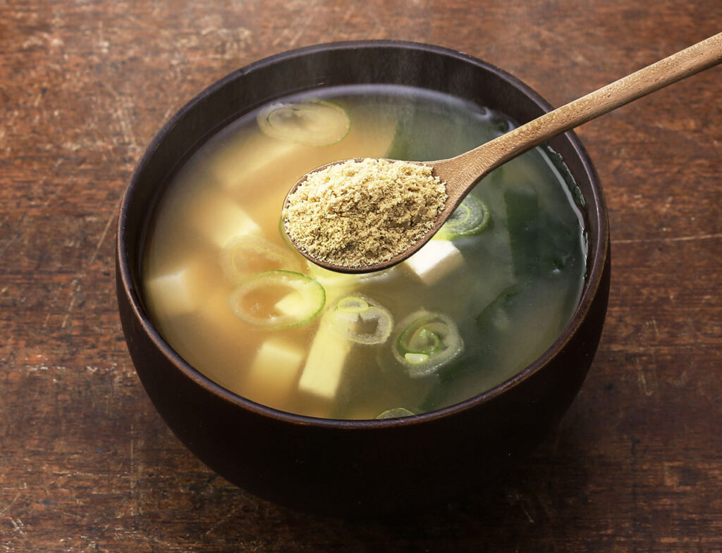 豆腐とねぎのお味噌汁に粉なっとうをふりかけようとする写真